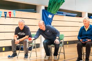 Man in chair throws a ball as two more people also sitting watch on
